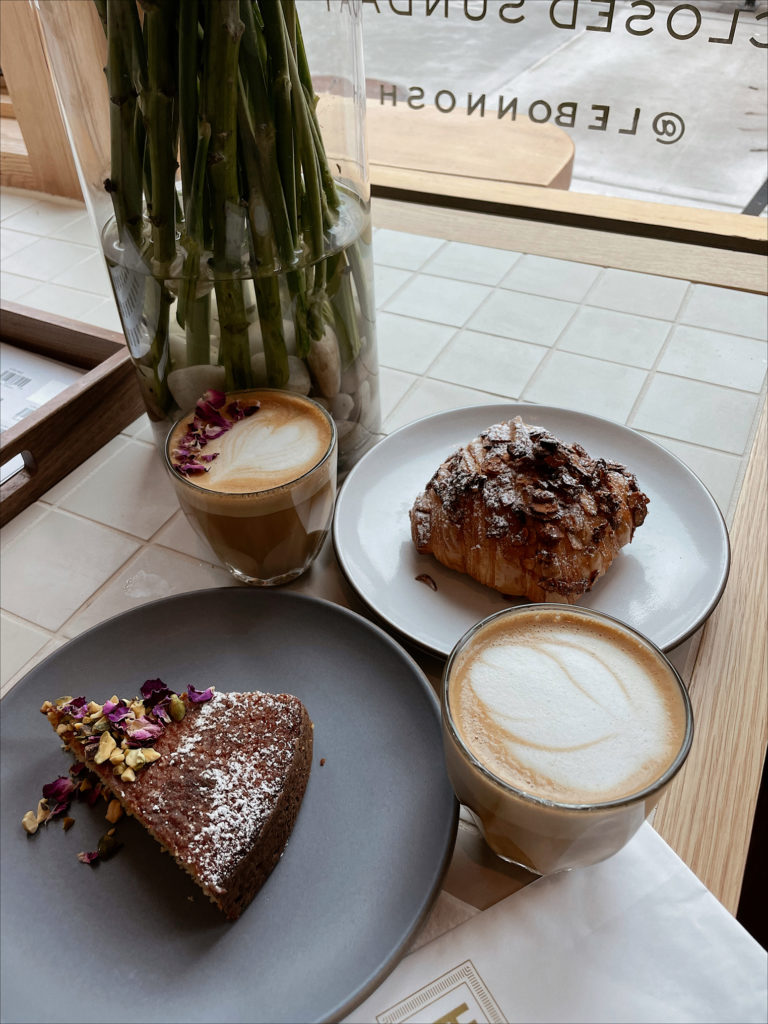 A picture of the rose latte, cardamom cake, almond croissant, and oat latte at Le Bon Nosh, located in the Buckhead neighborhood of Atlanta.